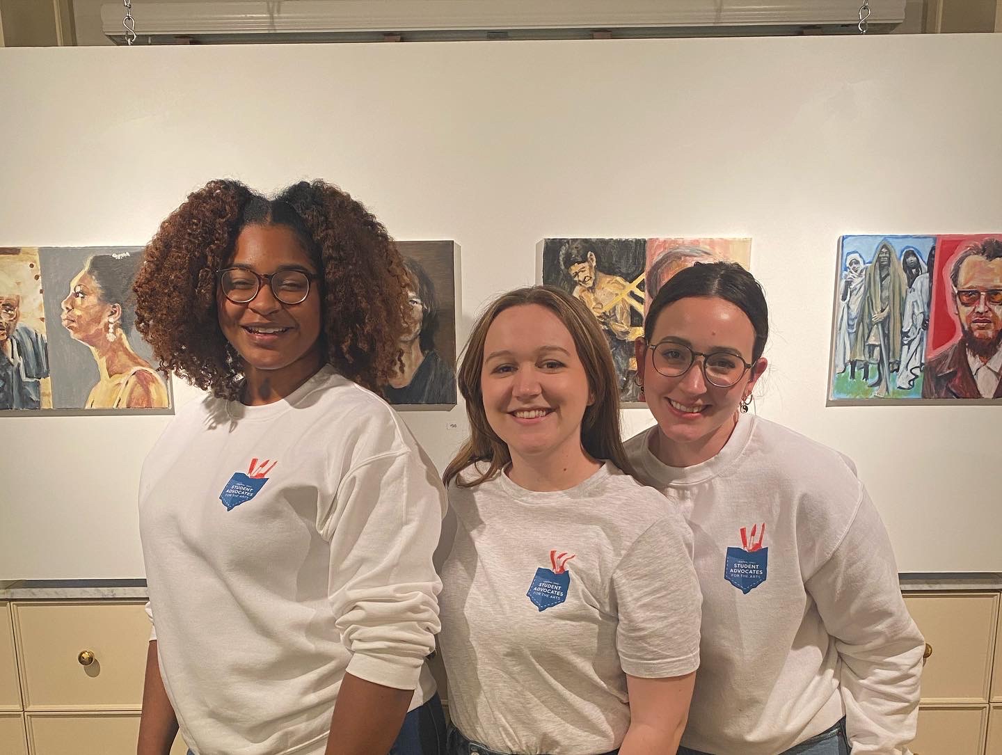 Three women wearing white shirts smiling at camera