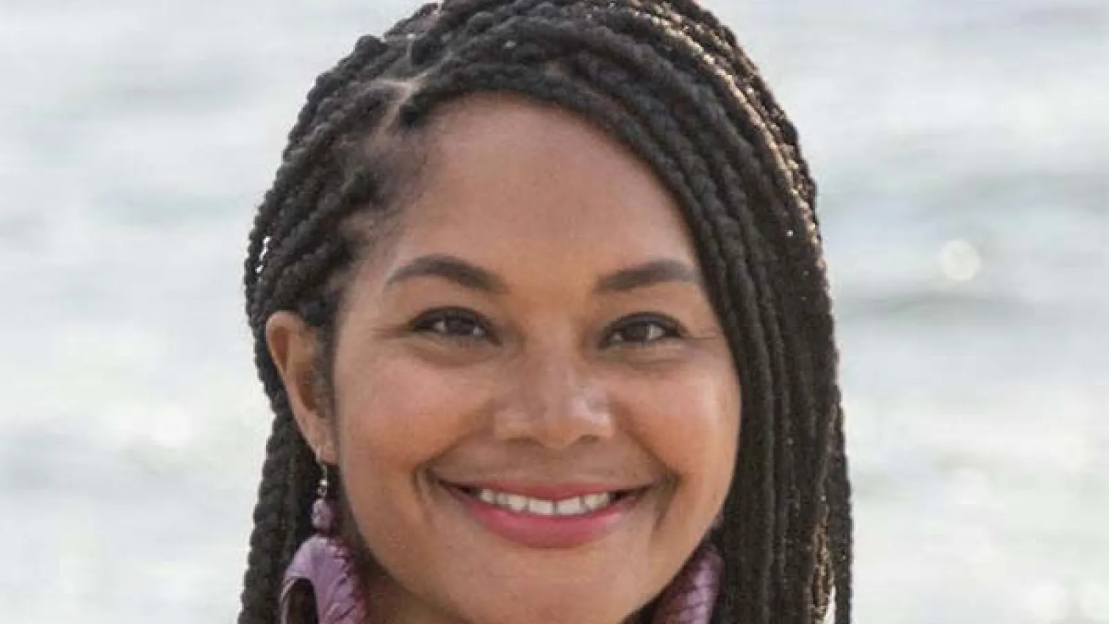Joni Acuff smiles at camera standing in front of water