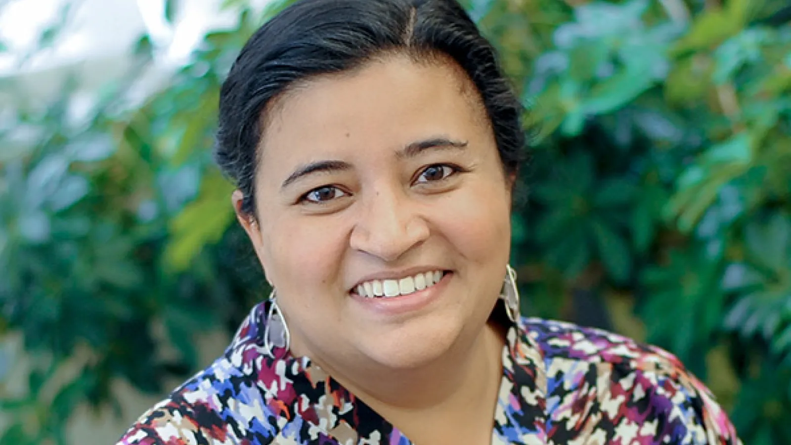 Dr. Patel smiles at camera in front of green plant