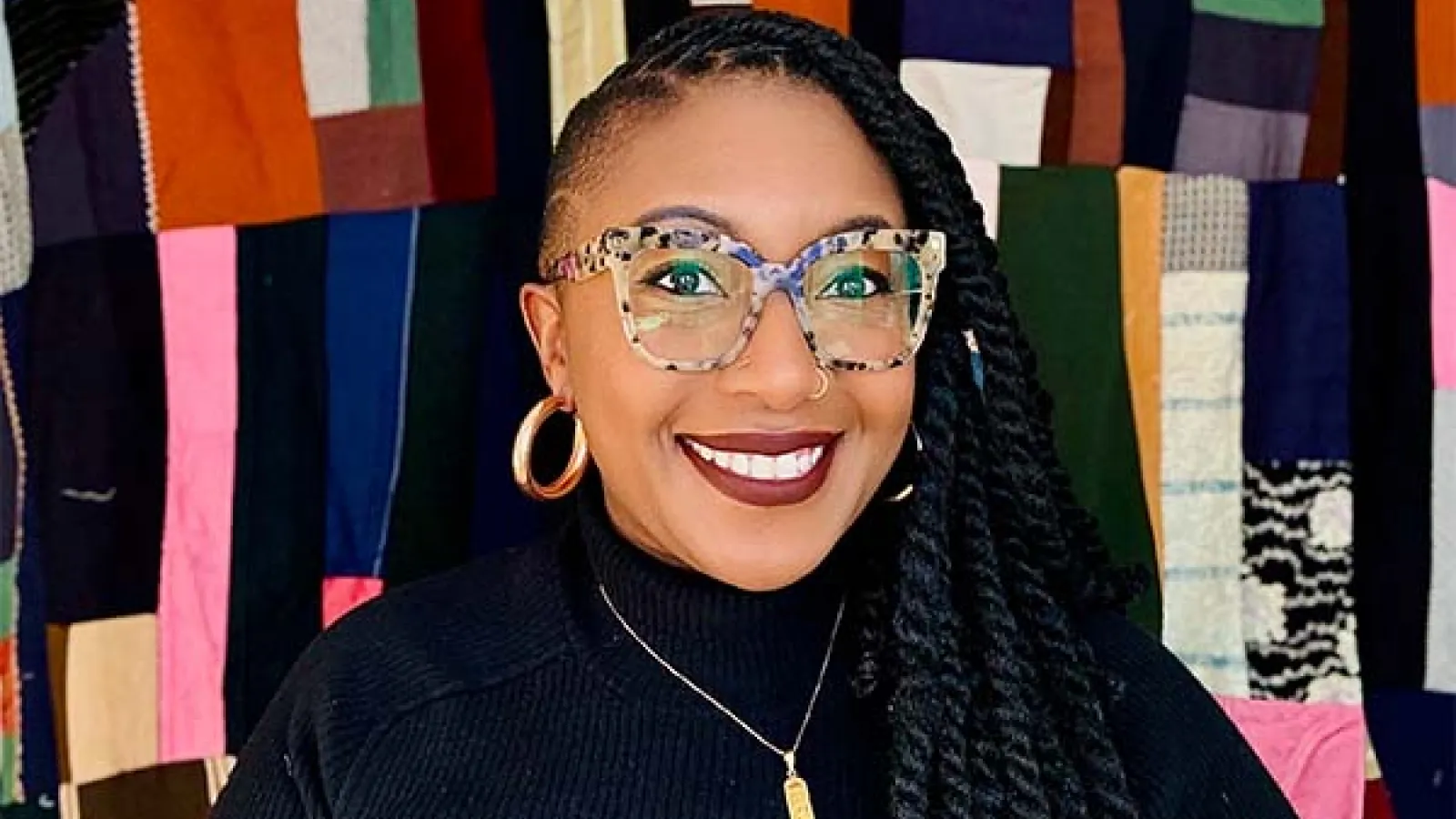 Sharbreon smiles at camera in front of colorful fiber art