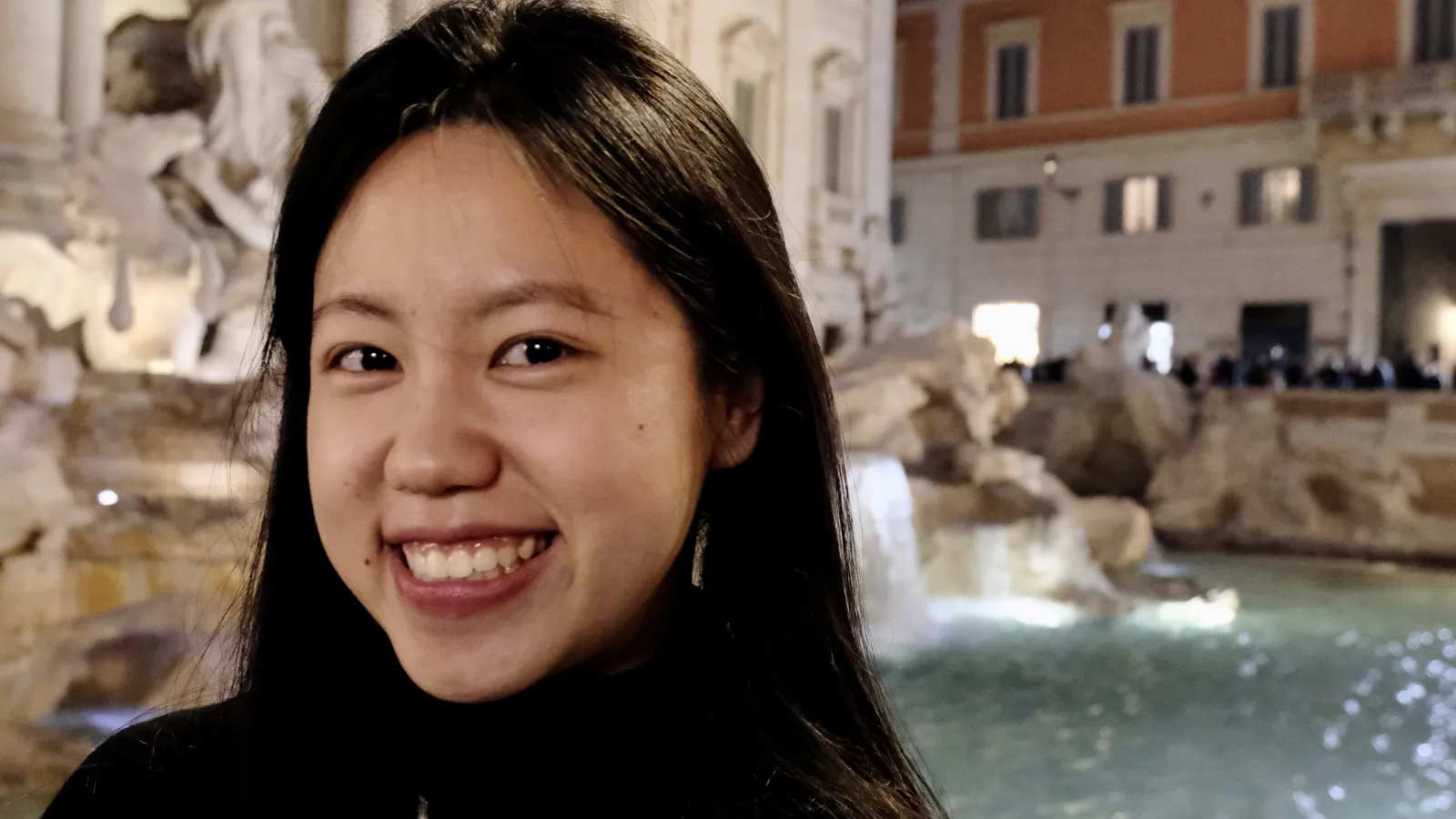 A woman smiling at the camera in front of a fountain