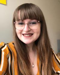 Woman with glasses and bangs, wearing striped shirt, smiling at camera