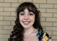 A woman with curly brown hair standing in front of a brick wall