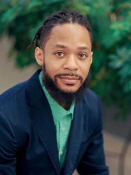 Man wearing green shirt and suit jacket, looking at camera