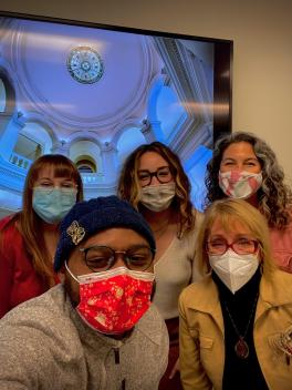 Four students and their instructor wearing masks, standing in front of a TV with a rotunda in the image