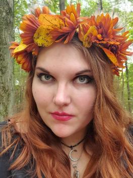 Woman with red hair and floral crown looks at camera
