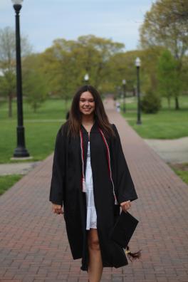 Caroline Bootes stands outside on brick pathway wearing graduation gown