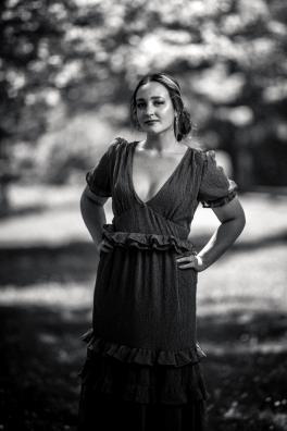 Black and white photo of Emily Hutlock standing in wooded area with hands on hips and hair pulled back in low bun