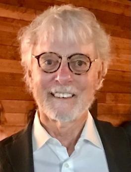 Man with glasses and white hair smiling at camera