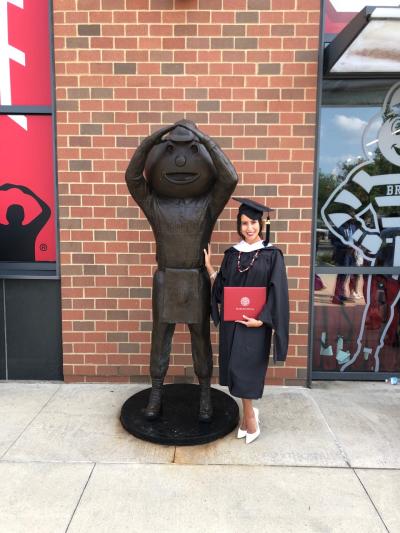 Tatiana Piche holding her diploma next to a Brutus Buckeye statue
