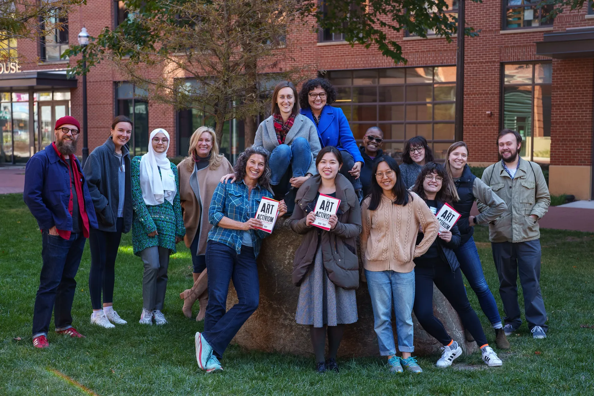 A group of students stand together holding books while smiling at camera