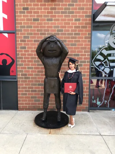 Tatiana Piche holding her diploma next to a Brutus Buckeye statue