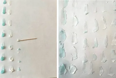 A series of toothpaste blobs line vertically along the left side of a piece of paper, a toothpick lays horizontally in the center of the paper. A series of aqua and white toothpaste blobs cover a piece of white paper.