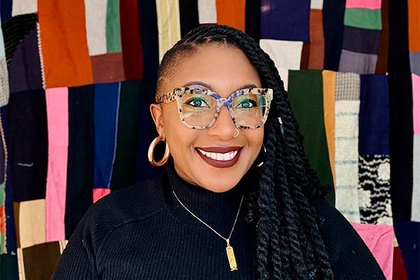 Sharbreon smiles at camera in front of colorful fiber art