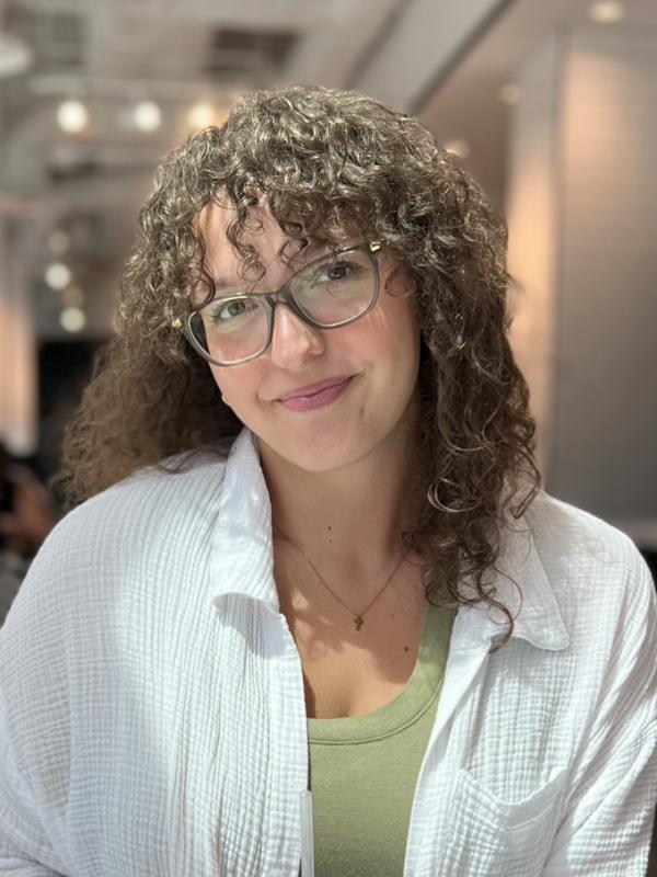 Woman in glasses with curly hair wearing white shirt looking at camera