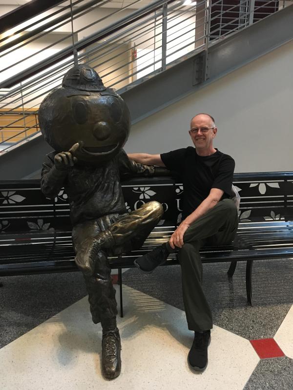 Peter Freeman sitting on a bench with statue of Brutus Buckeye