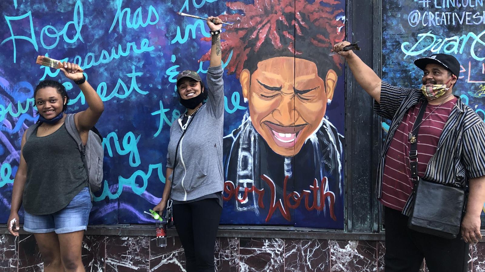 Artists stand in front of colorful mural