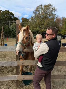 Man holding a baby as they stand by a horse
