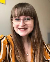Woman with glasses and bangs, wearing striped shirt, smiling at camera